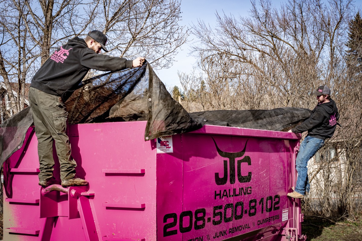 JTC crew tarping a loaded pink dumpster before hauling