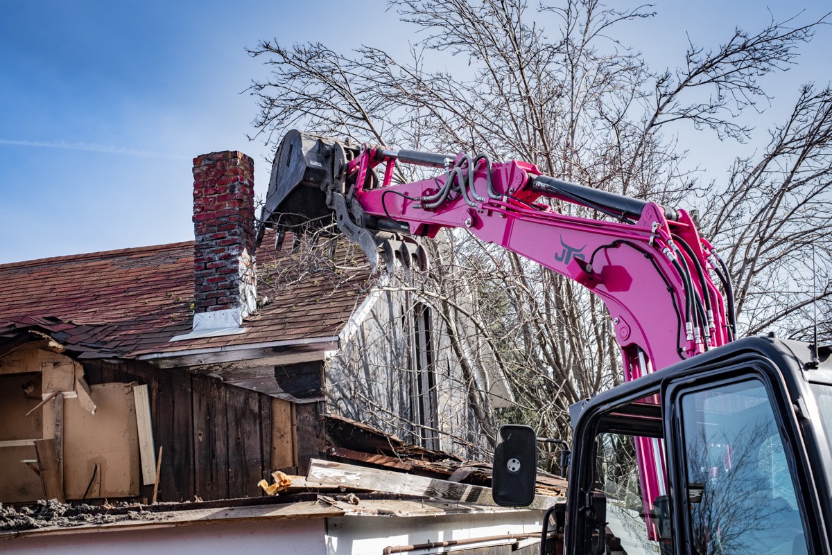 Excavator working over the chimney of a partially demolished house